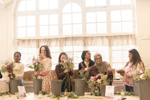 Group of women participating in a floral arrangement workshop in a bright room with large windows.